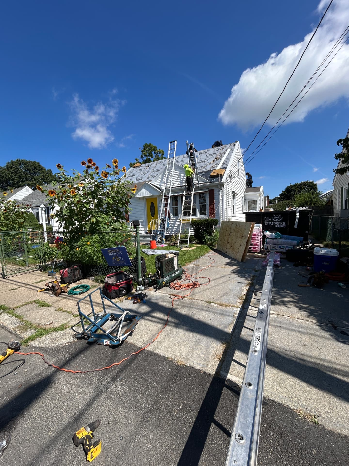 Roof replacement in progress with ladders, dumpster and underlayment on a Rhode Island home