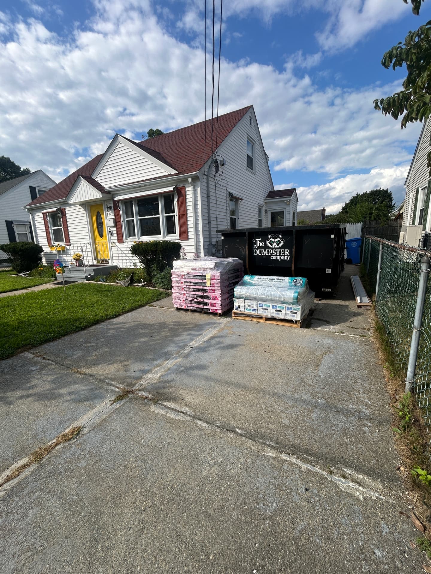 Roofing materials and dumpster staged in the driveway before a roof replacement