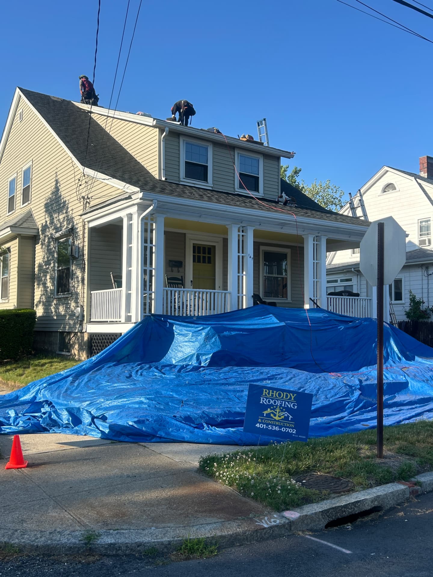 Rhody Roofing crew replacing the roof on a Rhode Island home with tarps protecting the yard